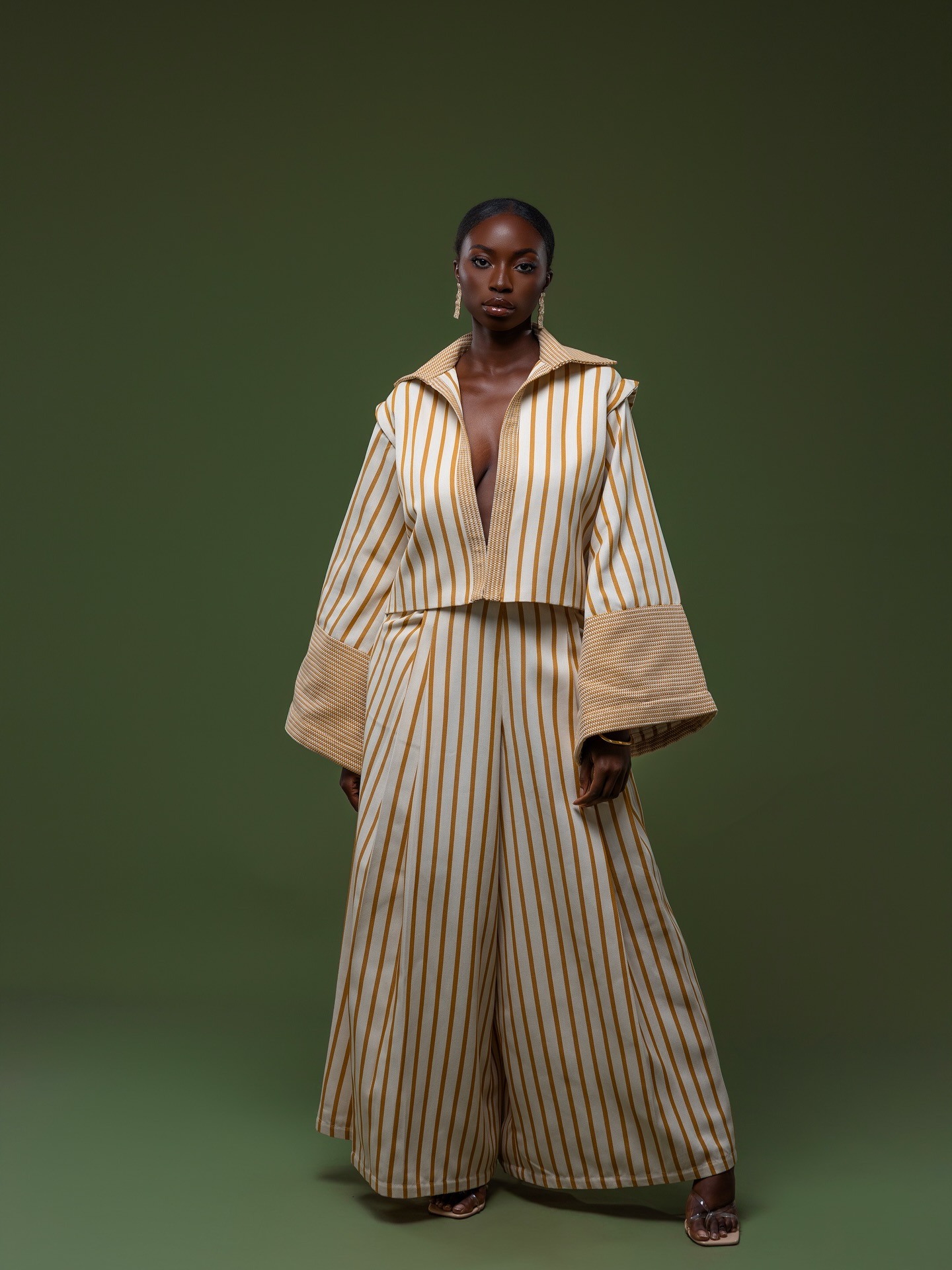Ensemble rayé ivoire et ocre — veste courte à poignets tressés et pantalon palazzo, fond vert forêt.