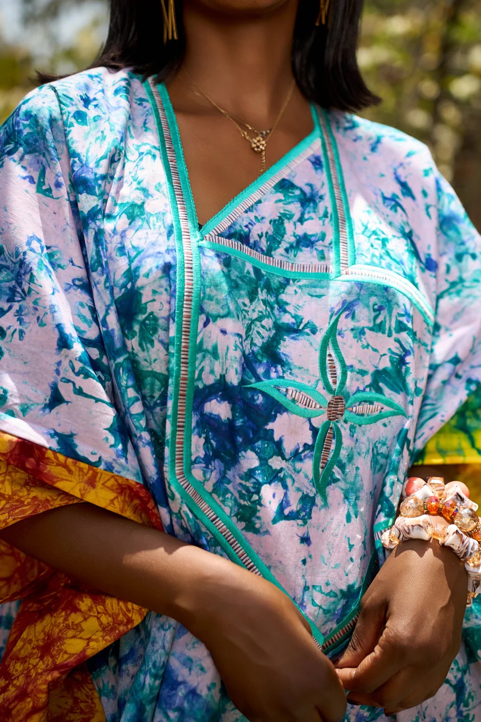 Gros plan sur la broderie fleur et le col en V d'un kaftan bleu marbré.