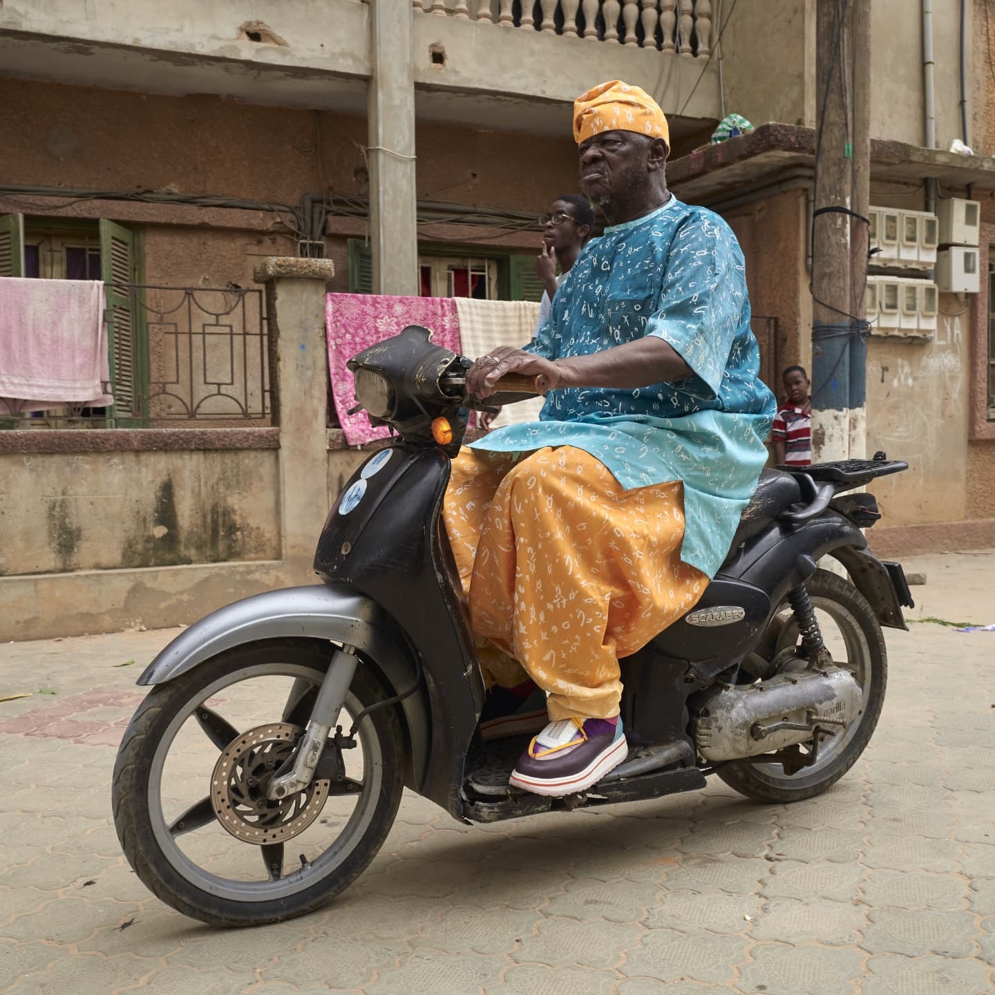 Ancien en boubou imprimé sur scooter — Dakar street