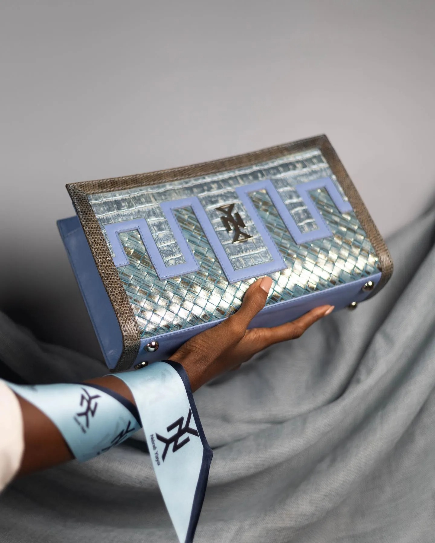 Pochette rigide métallisée bleu ciel — tressage main, incrustation lézard et carré signature