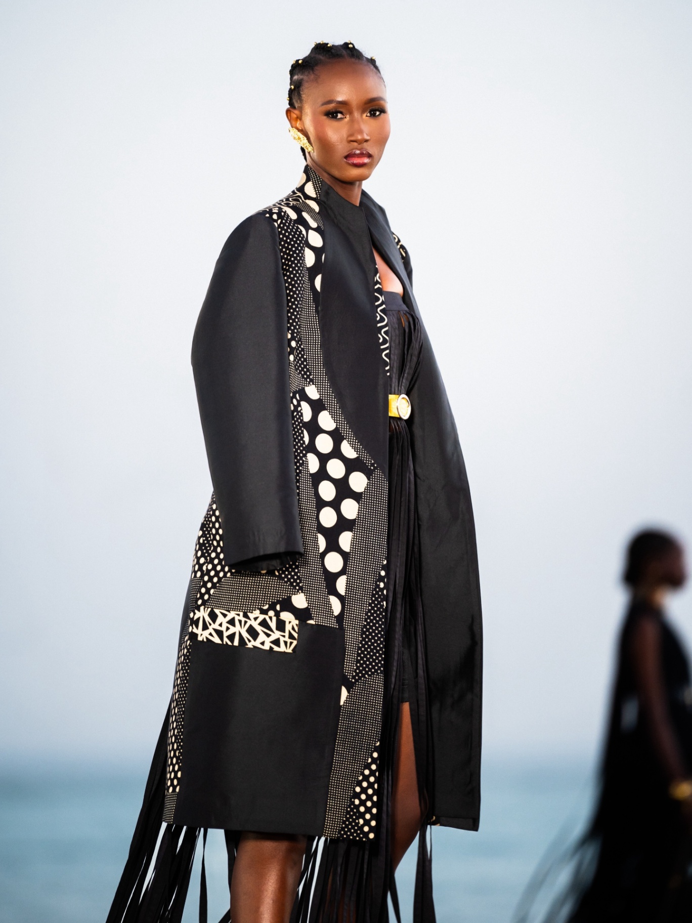 Manteau ceinturé à boucle dorée, franges fluides et pois contrastés.